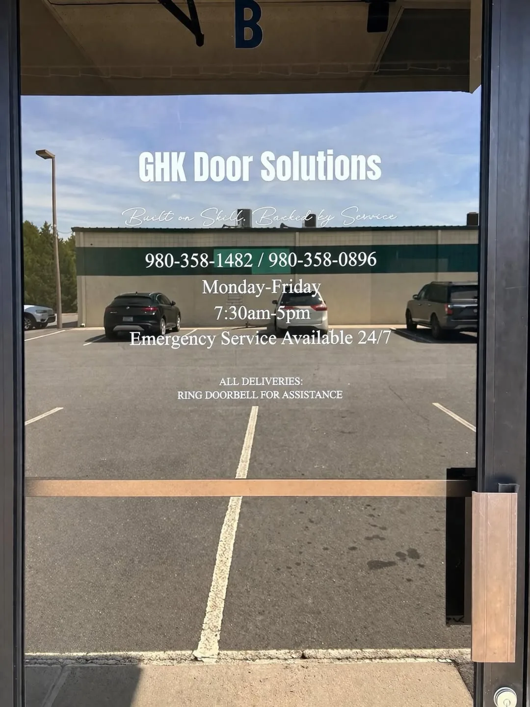 GHK Door Solutions branded storefront entry with hours and 24/7 emergency service notice